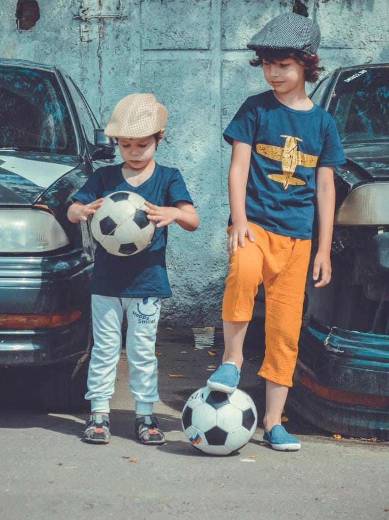 pexels-photo-1564868-1564868 Two children in casual attire play soccer near vintage cars on a sunny day.